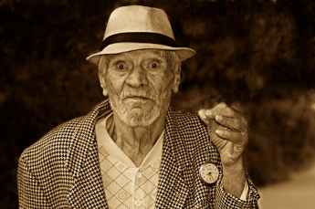 grayscale photo of a man in houndstooth print suit jacket wearing a hat